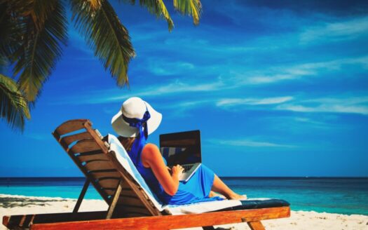 Remote worker in Greece using laptop outdoors overlooking beach, illustrating tips for remote working lifestyle in Greece.