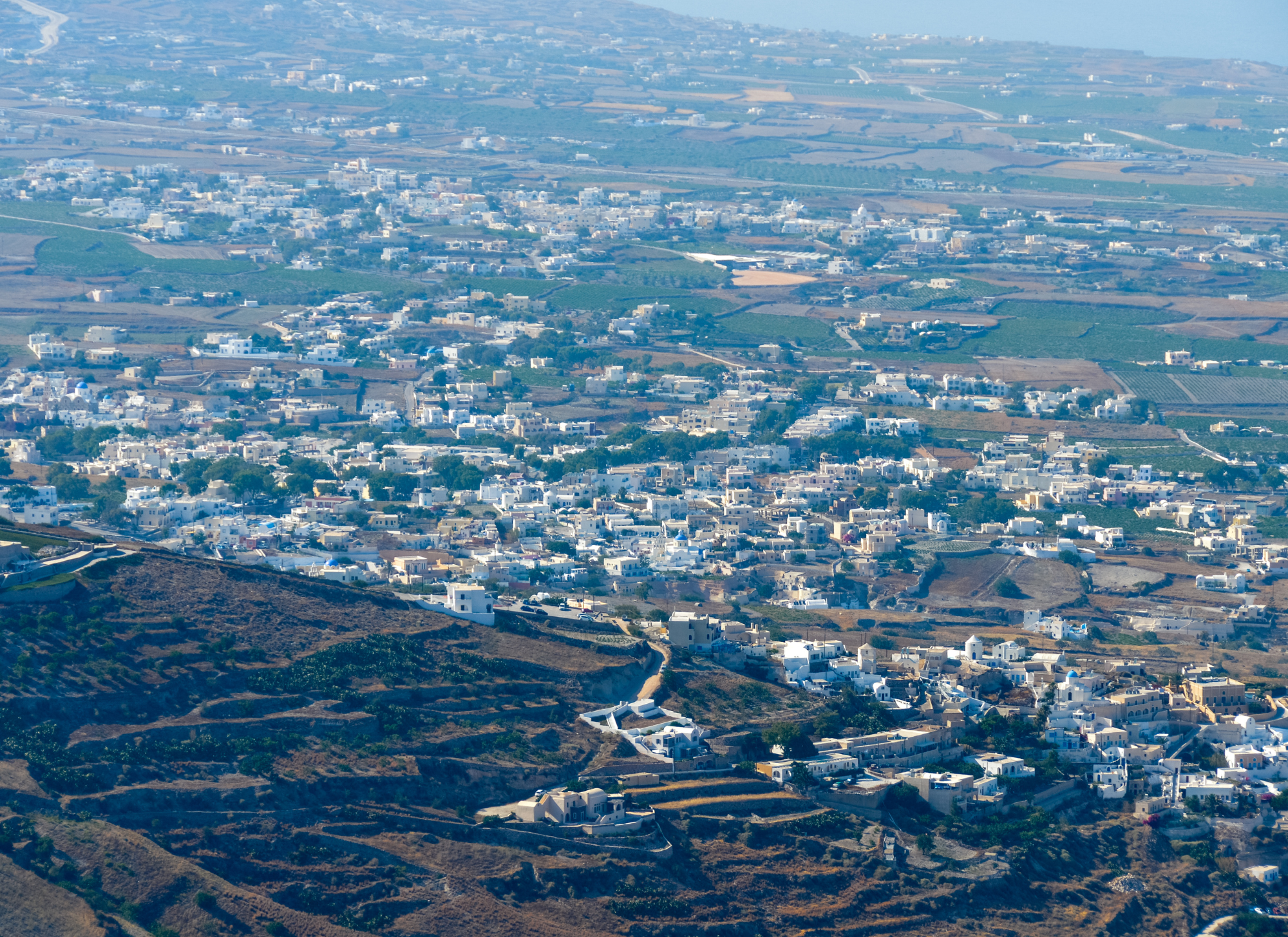 Aerial view of Santorini, Greece, showcasing its iconic white buildings and blue-domed churches, highlighting the impact of tourism on local real estate.