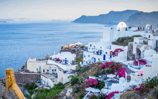 Real estate investment in Greece, showing a villa overlooking the sea with tourists enjoying the beach, reflecting 2025 tourism trends.