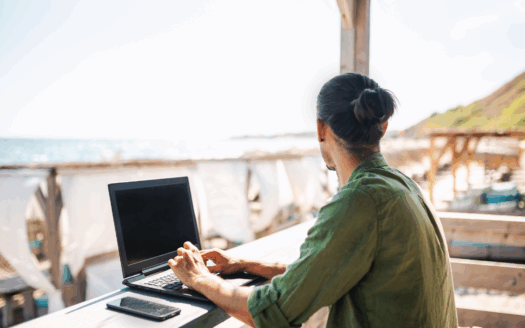 Digital nomad working remotely in Greece with a laptop overlooking the Mediterranean Sea.