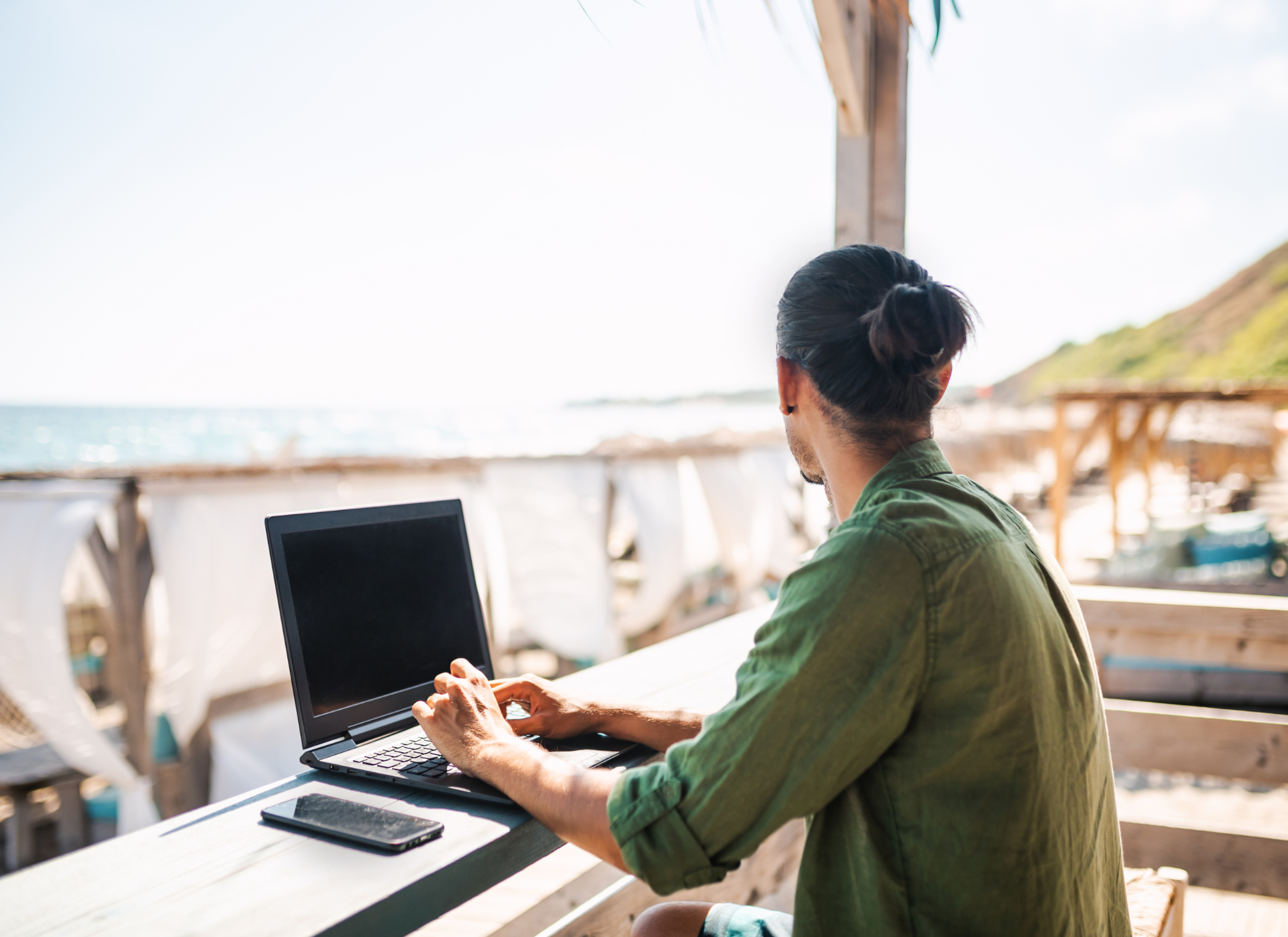 Digital nomad working remotely in Greece with a laptop overlooking the Mediterranean Sea.